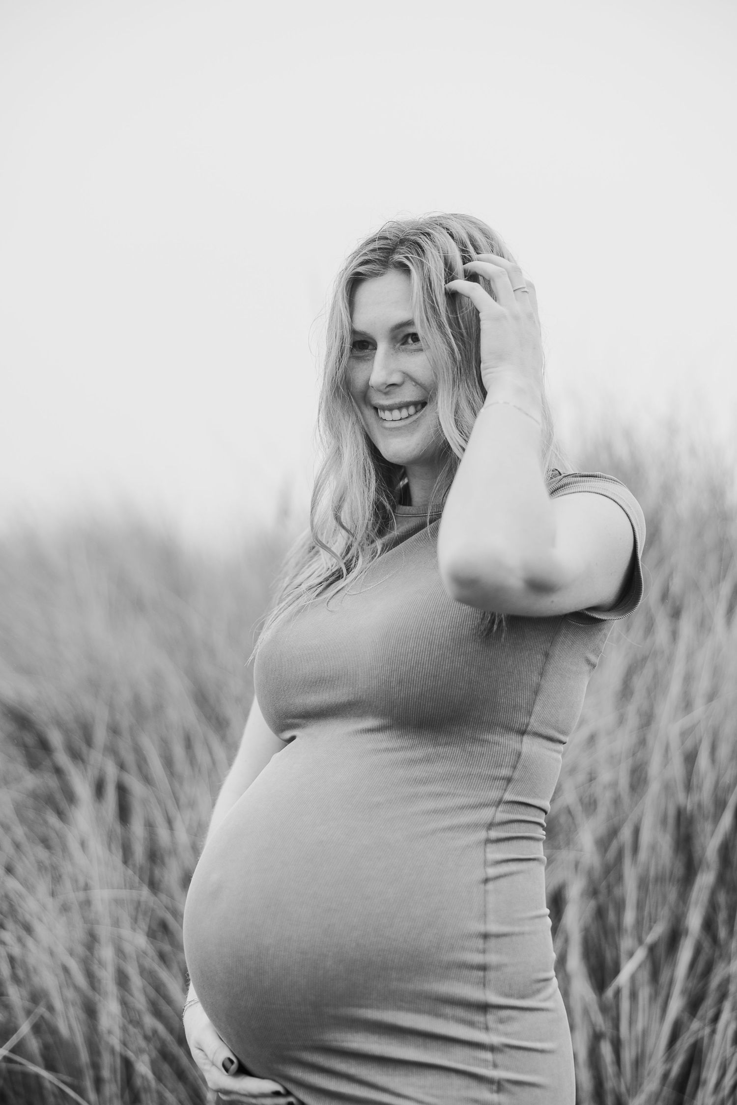Black and white maternity photo showing a joyful moment during a pregnancy photoshoot outdoors.