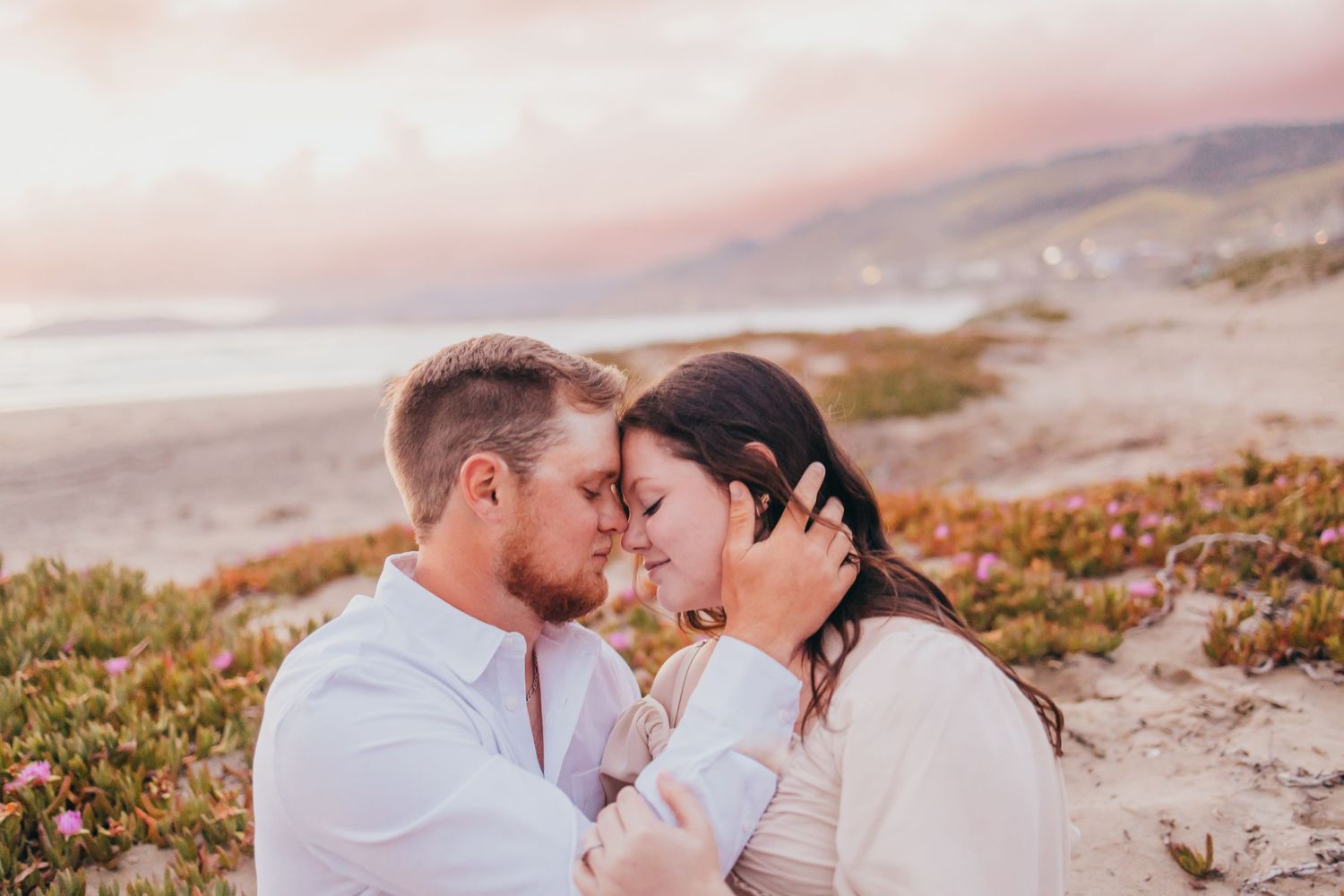 Romantic sunset portrait on coastal cliffs with soft pink sky.