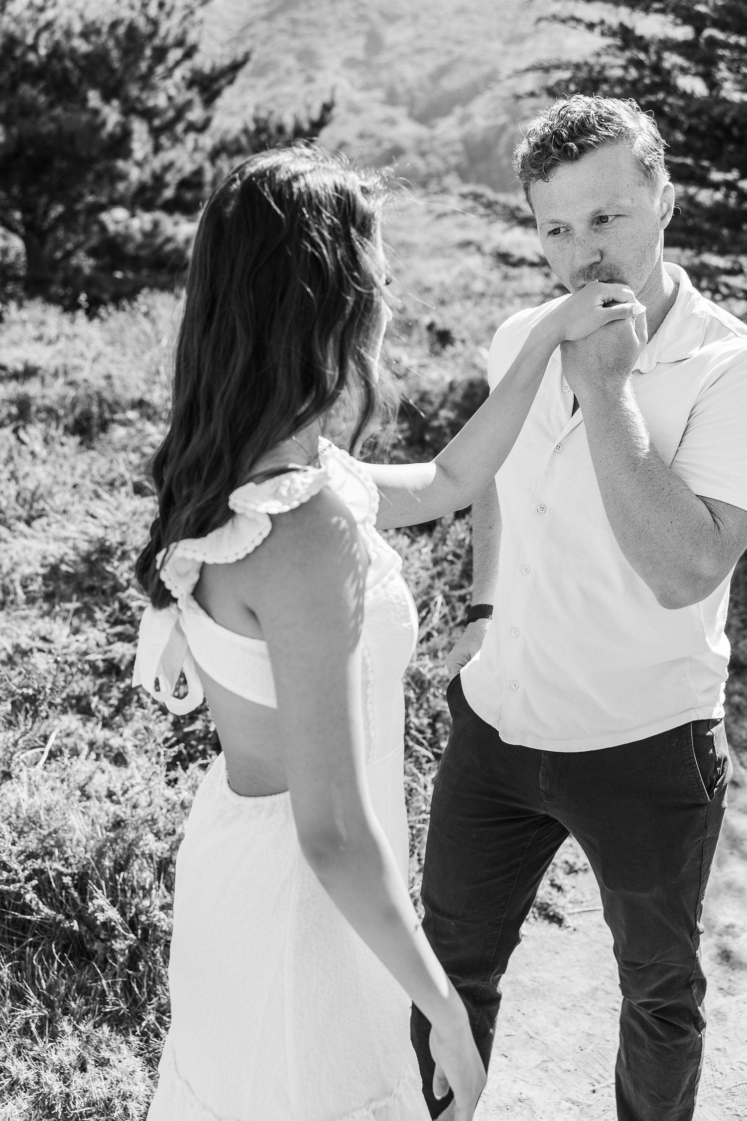 A romantic black and white moment between two people on a sunny hillside path.