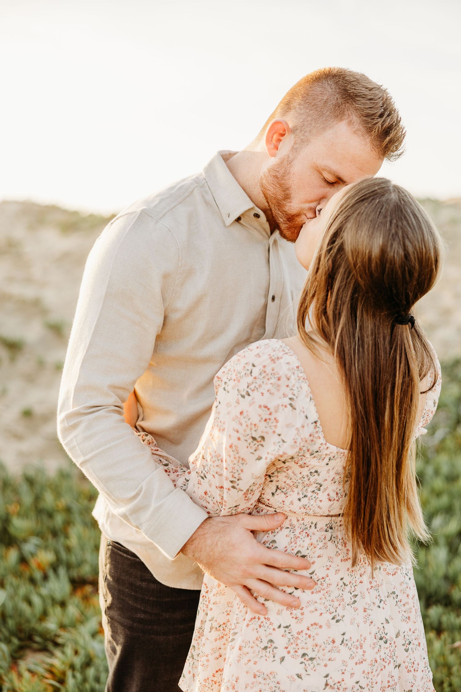 An intimate moment captured between a couple in floral dress and light colored shirt outdoors.