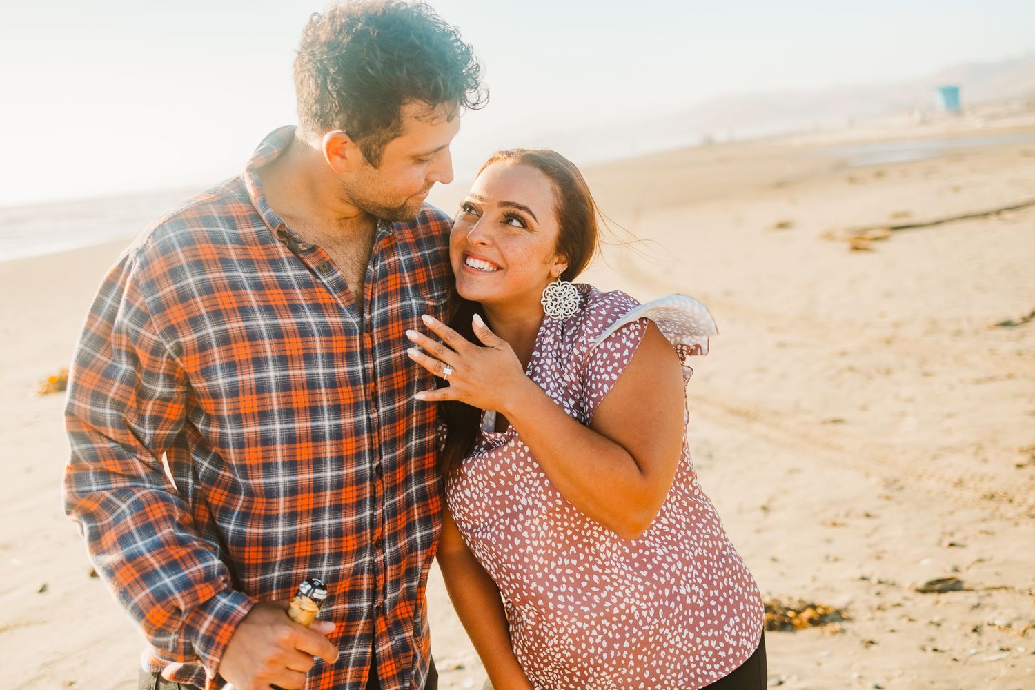 Happy couple enjoying a playful moment on sandy beach in coordinated casual outfits.