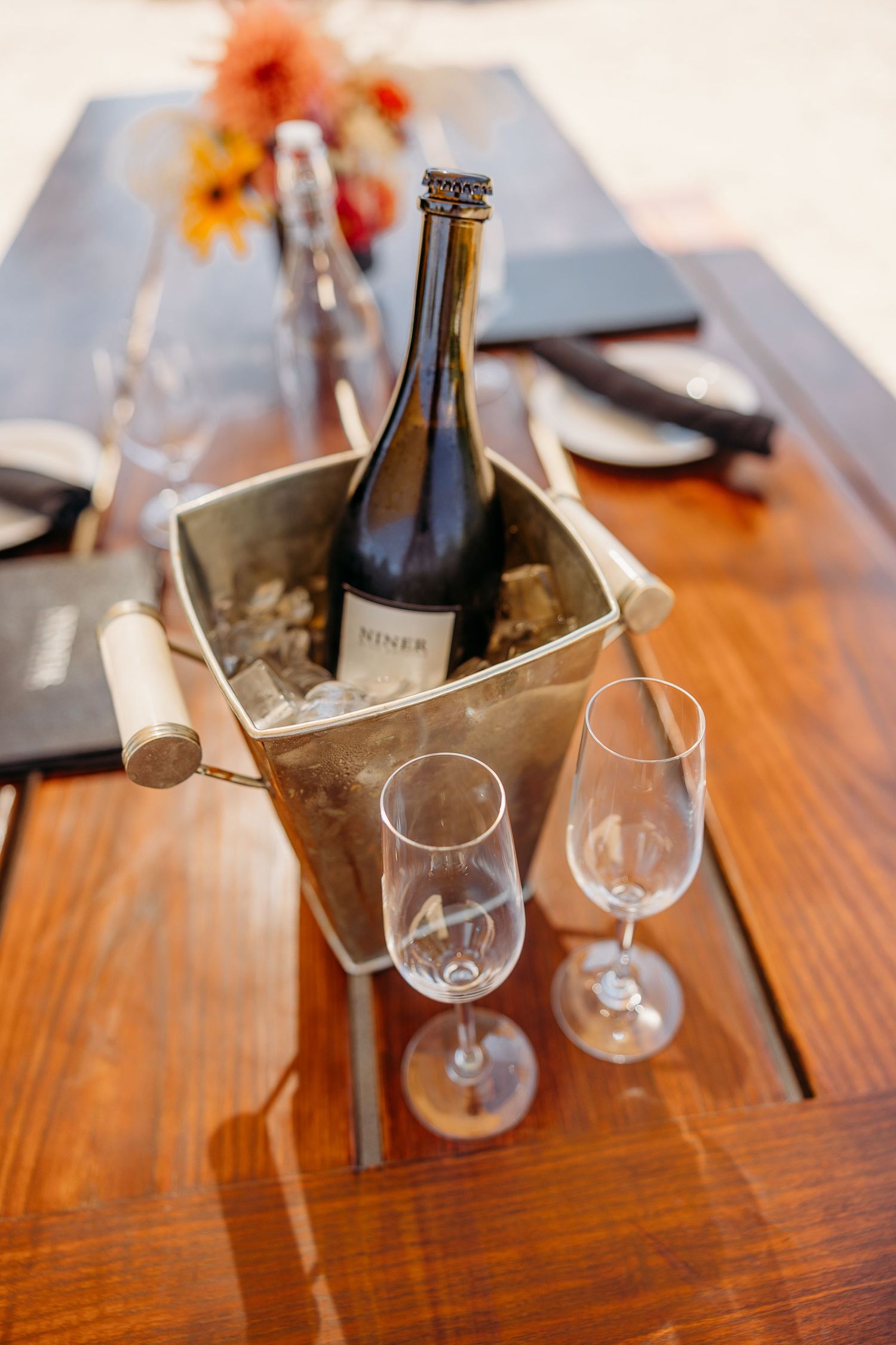 Wine glasses and bottles arranged on a polished wooden table at an outdoor dining setup.