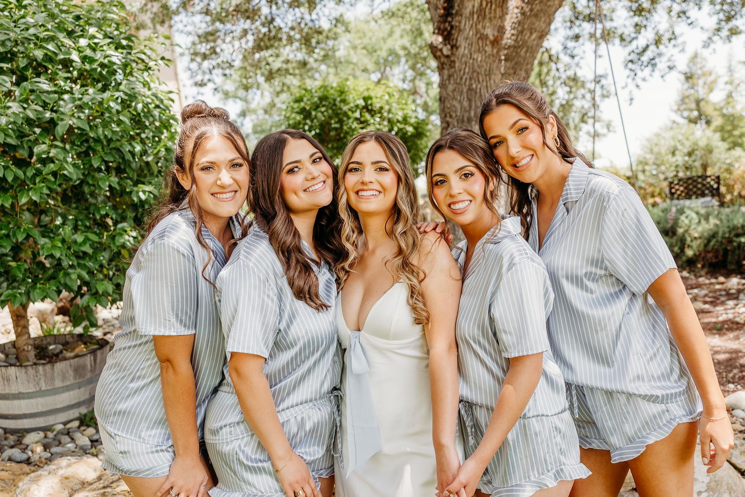 A group dressed in coordinating grey and white outfits pose together outdoors for a family photo session.