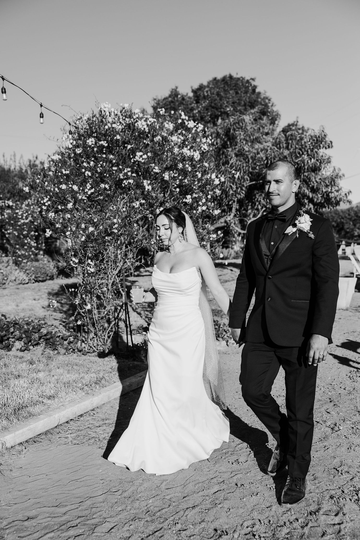 Black and white photo of newlyweds walking together on a garden path.