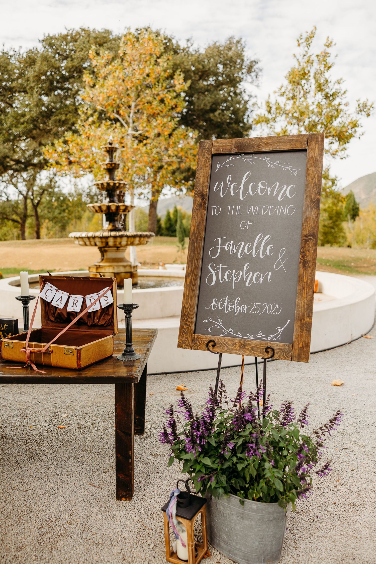 Rustic wooden welcome signs with chalkboard lettering and purple flowers in outdoor wedding decor.