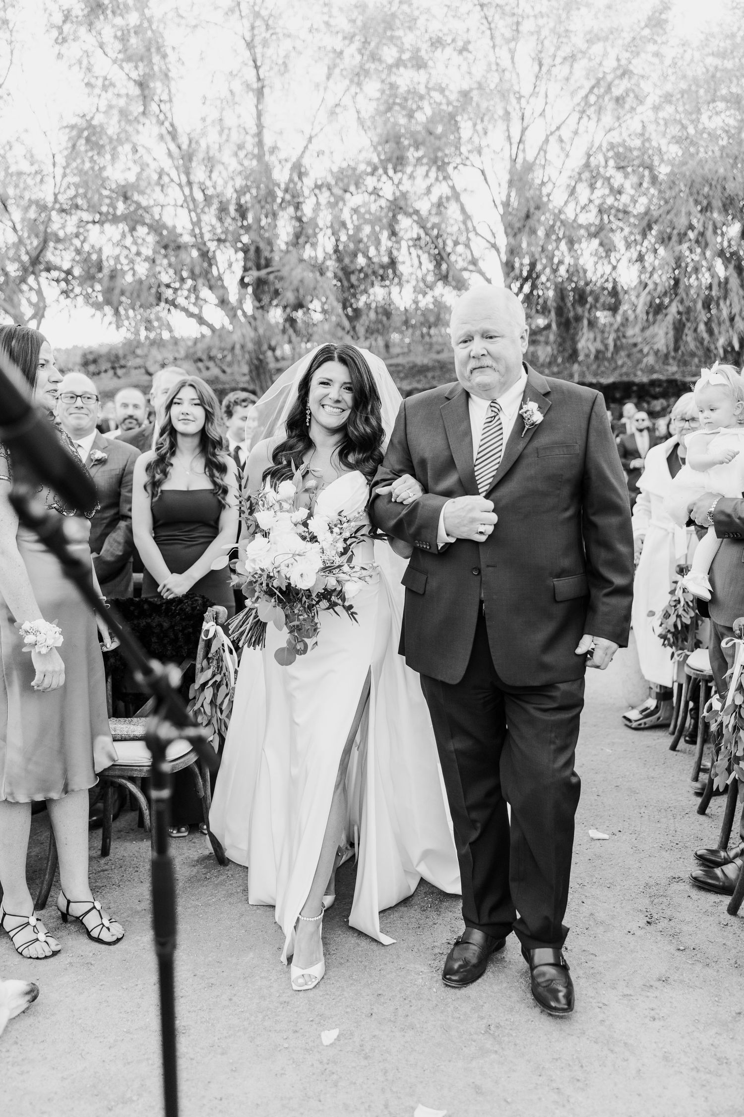 A traditional wedding ceremony processional taking place outdoors under trees.