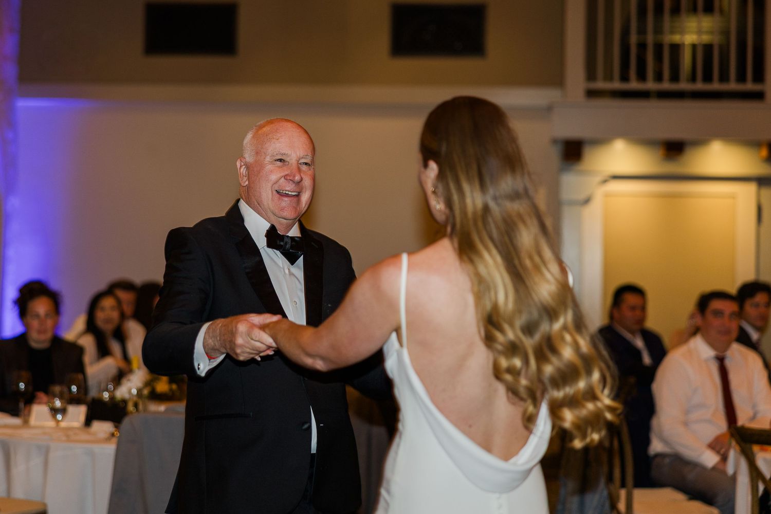 Wedding reception celebration with guests dancing under purple lighting in a banquet hall.