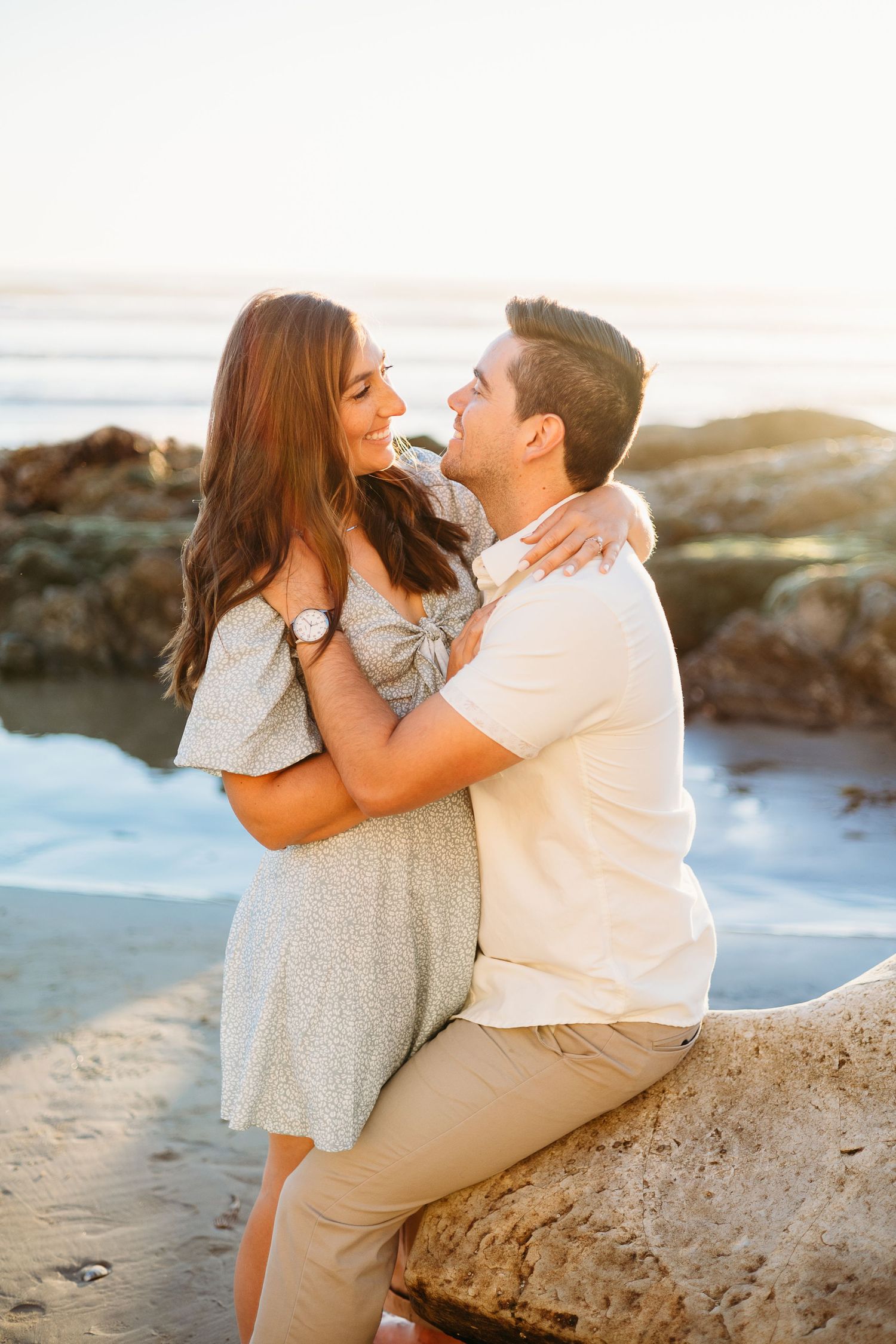A romantic couple poses on coastal rocks during a sunset photoshoot.
