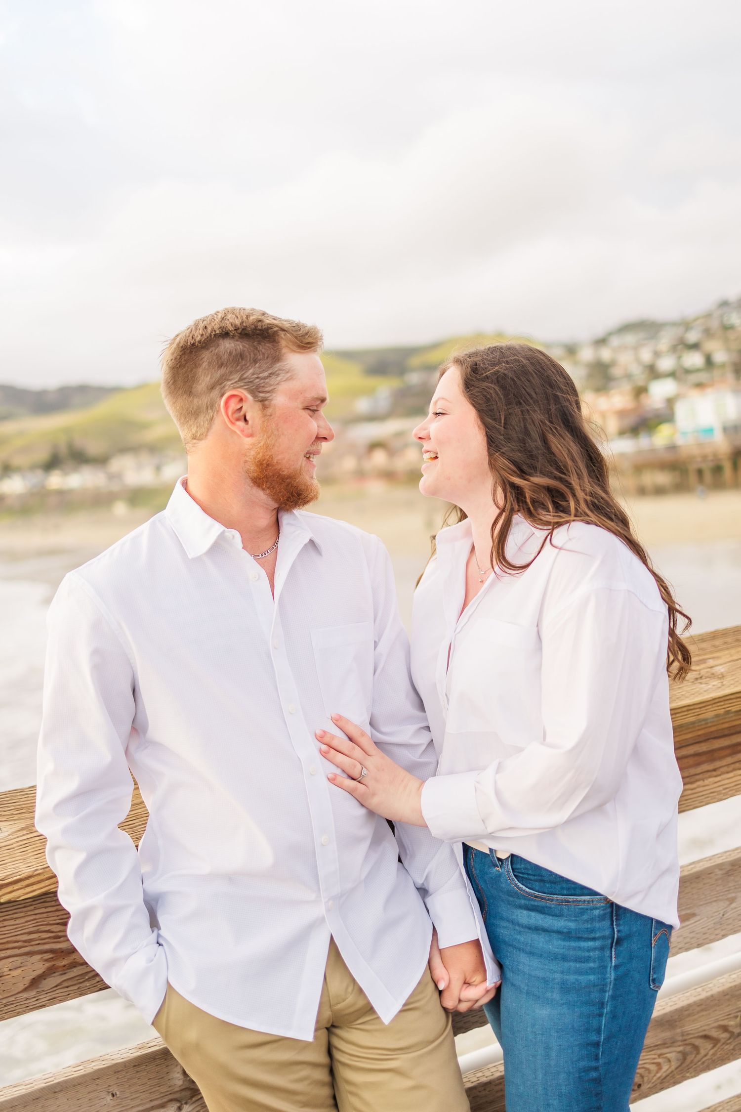 Couple in white shirts sharing romantic moment on wooden pier by ocean.