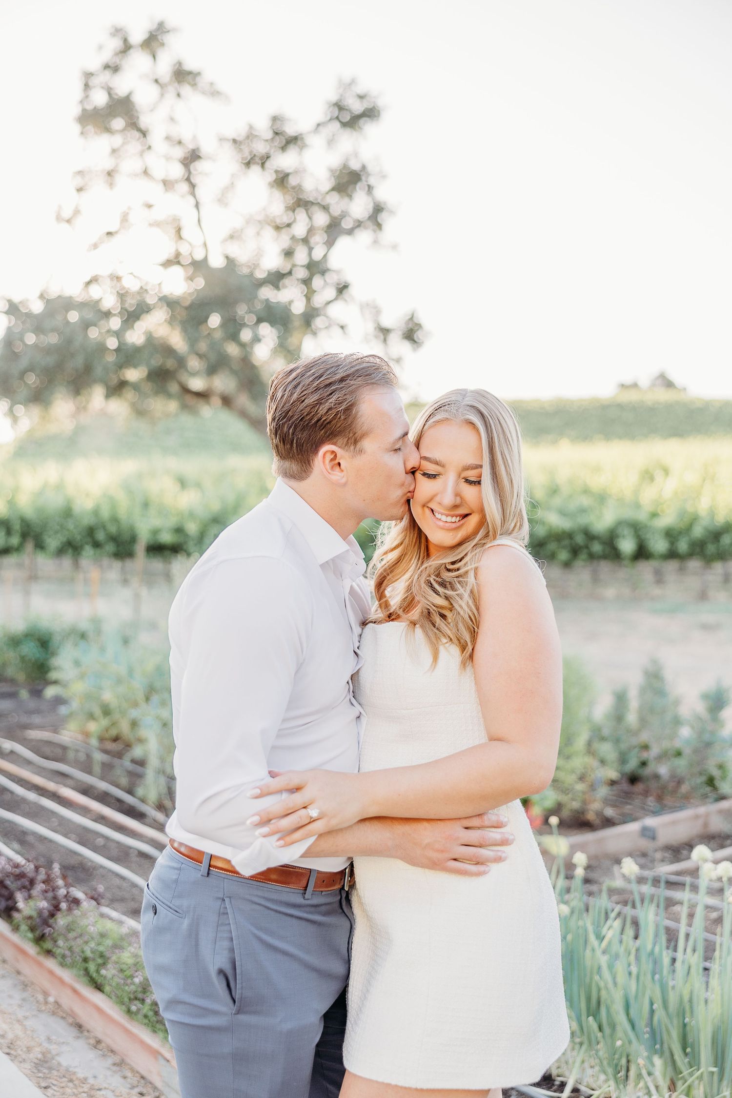 A joyful couple embraces in a sunny garden setting during their engagement photoshoot.