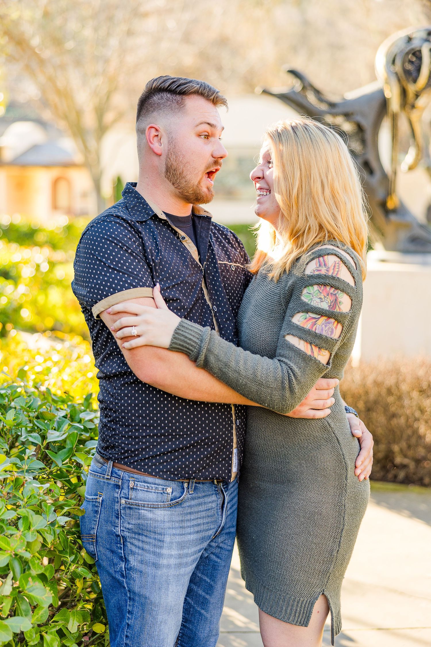 Couple sharing an intimate moment outdoors in front of sculpted garden bushes and a statue.