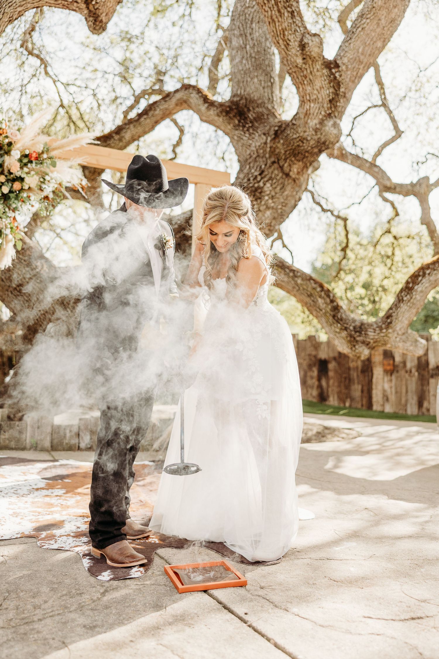Atmospheric smoke effect creates dreamy ambiance during outdoor wedding photography session under large tree.
