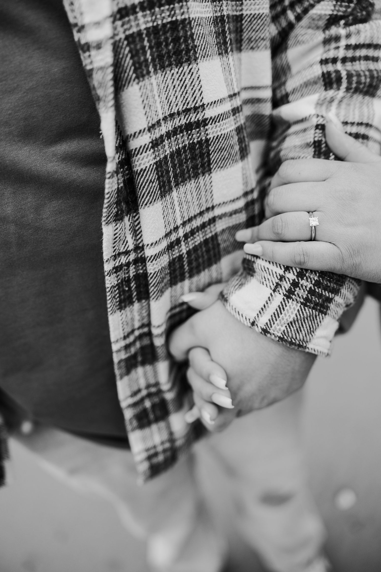 Black and white close-up of hands holding each other, with one person wearing a plaid flannel shirt and a ring.