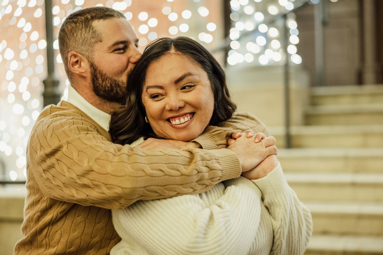 A couple embraces and laughs together during an outdoor engagement photo session with warm lighting.