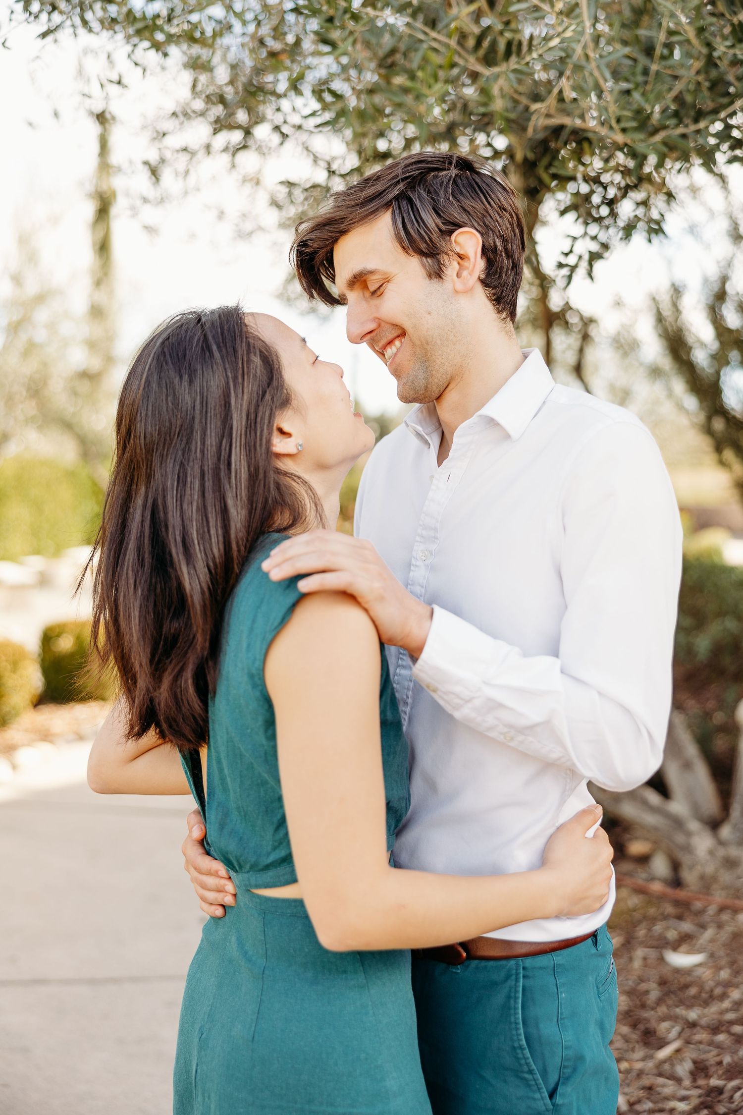 A romantic couple embraces tenderly in a garden setting, wearing a green dress and white shirt.