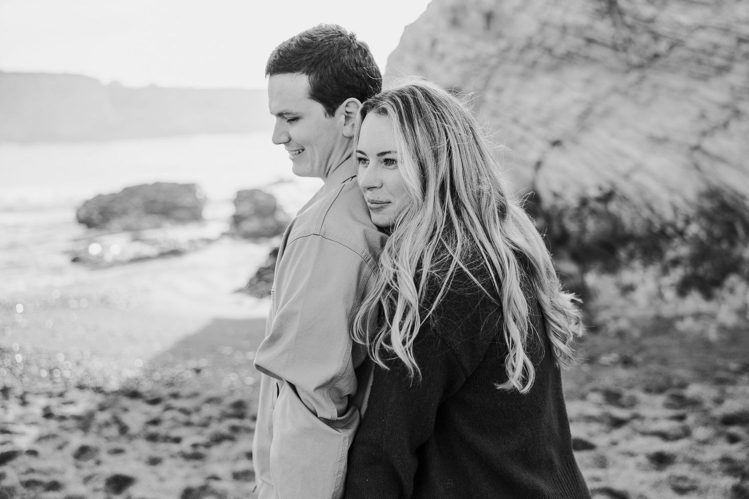 Couple sharing tender moments along dramatic coastal cliffs in black and white.