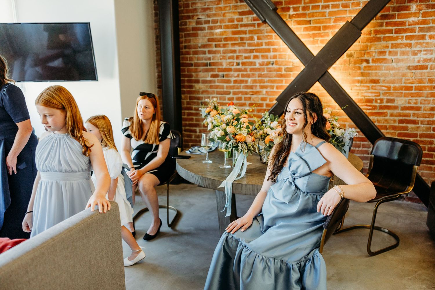 Wedding guests gather in an industrial-style venue with exposed brick walls and modern furnishings.