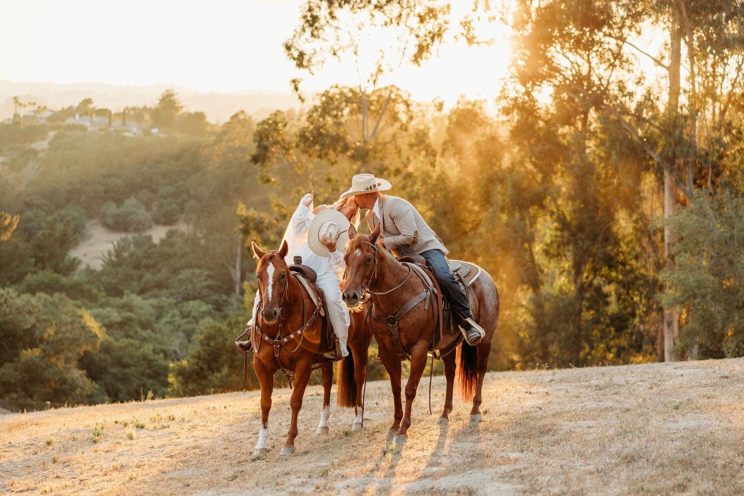 Two horses and riders silhouetted against a golden sunset through trees.