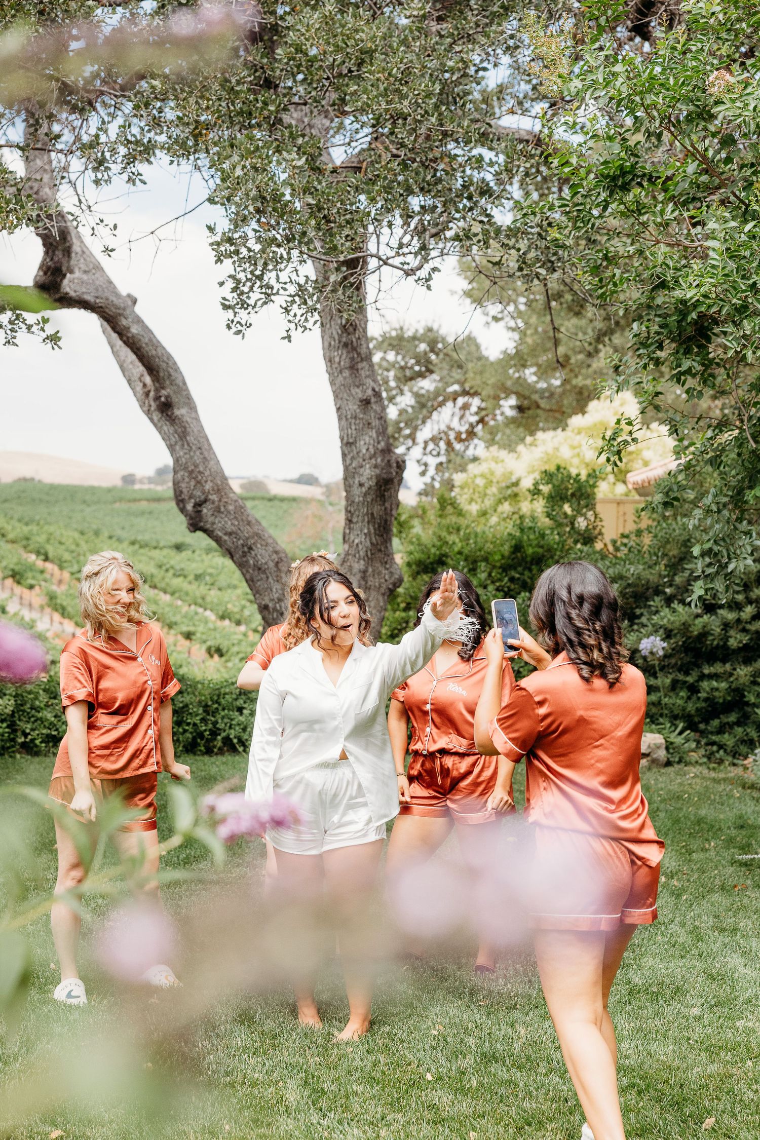 Group celebrating outdoors in orange robes among olive trees and gardens.