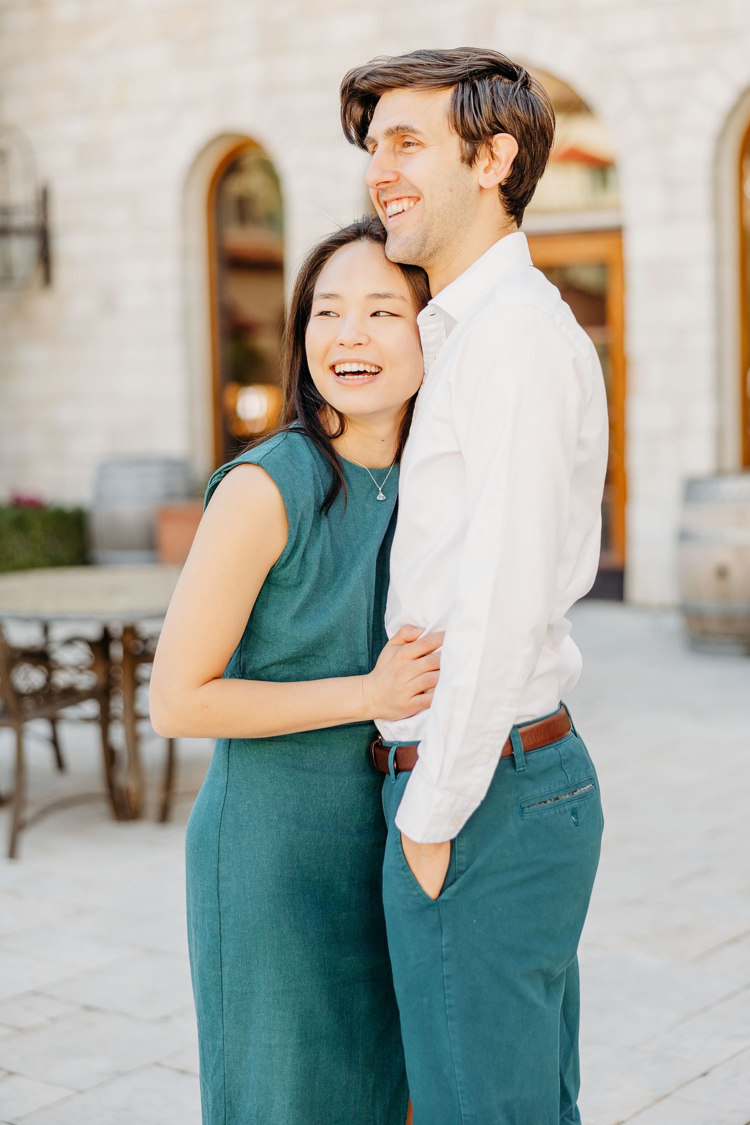 A couple shares a joyful embrace while wearing coordinating outfits of white and teal against a stone building.