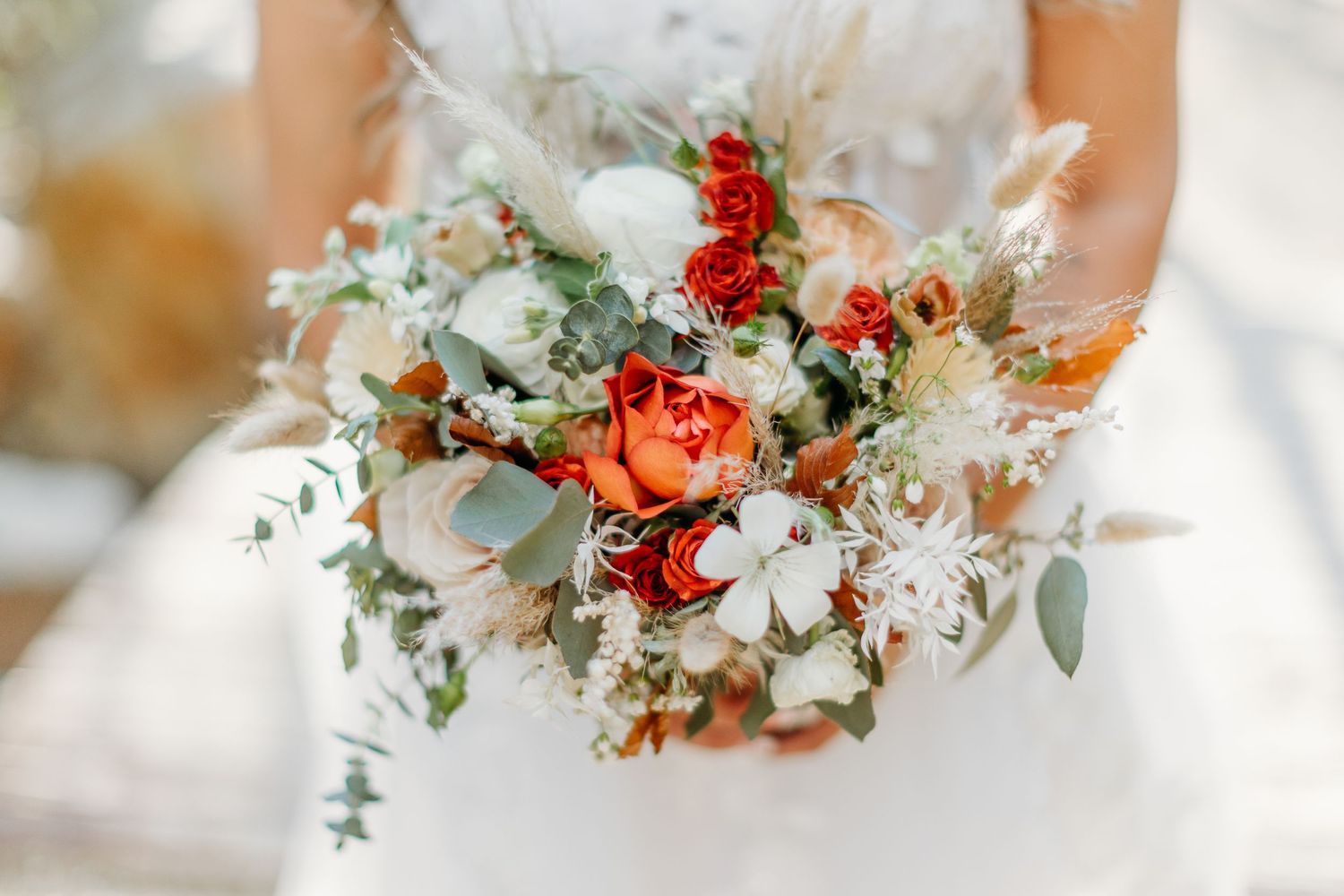 A romantic wedding bouquet with white and coral flowers, featuring eucalyptus leaves and delicate dried elements.