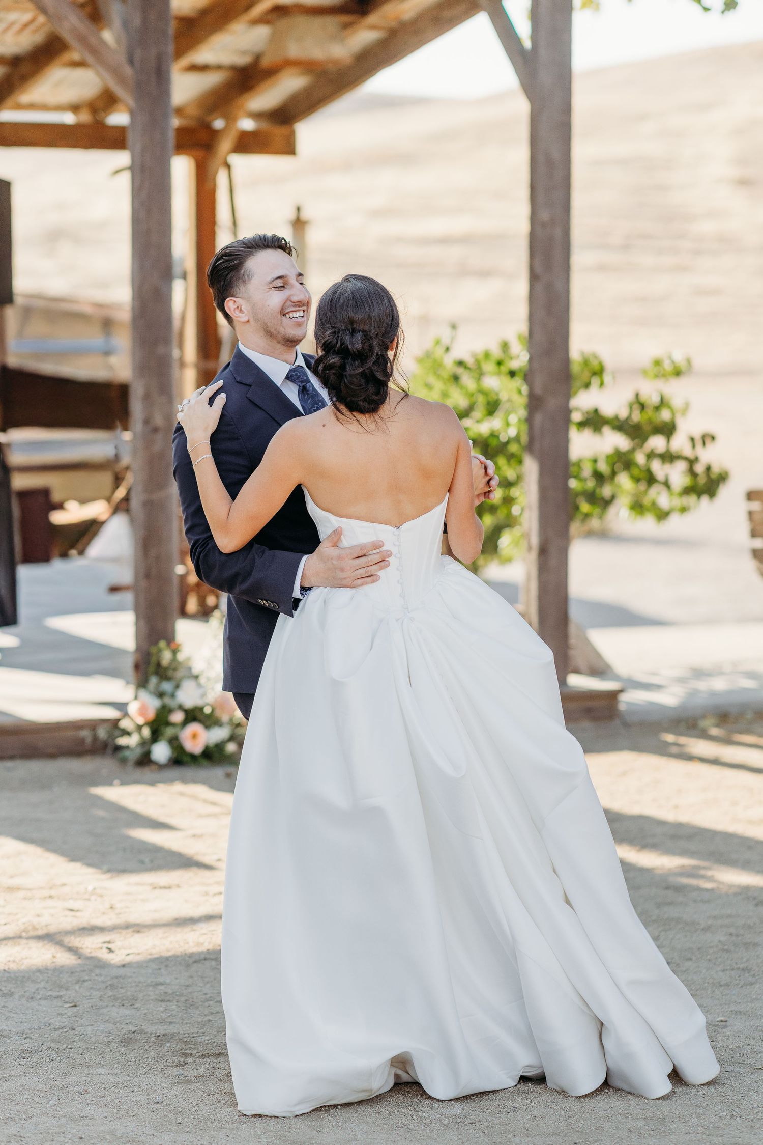 A couple shares an intimate moment on their wedding day under a rustic wooden pergola.