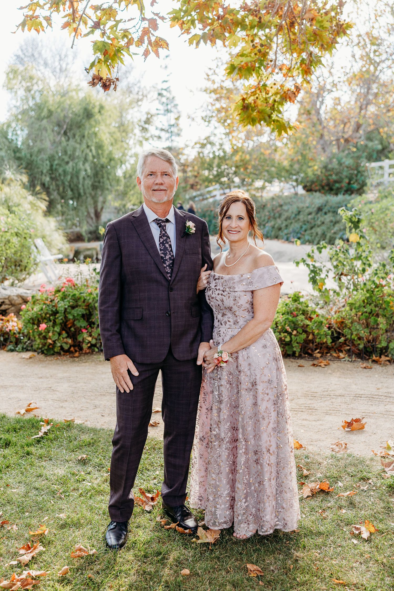Wedding party members pose together on autumn grounds with fallen leaves.
