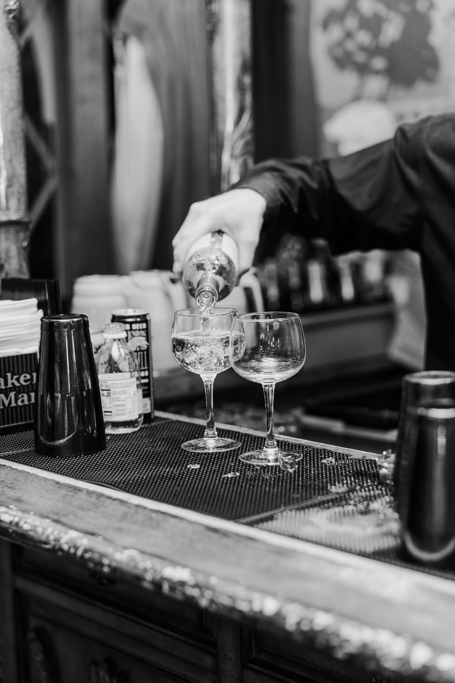Black and white photo of empty cocktail glasses on a bar with bottles in the background.