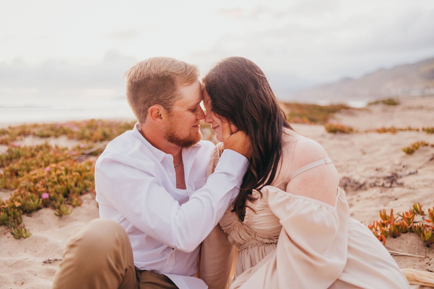 Intimate couple's portrait session on sandy beach with golden sunset lighting.