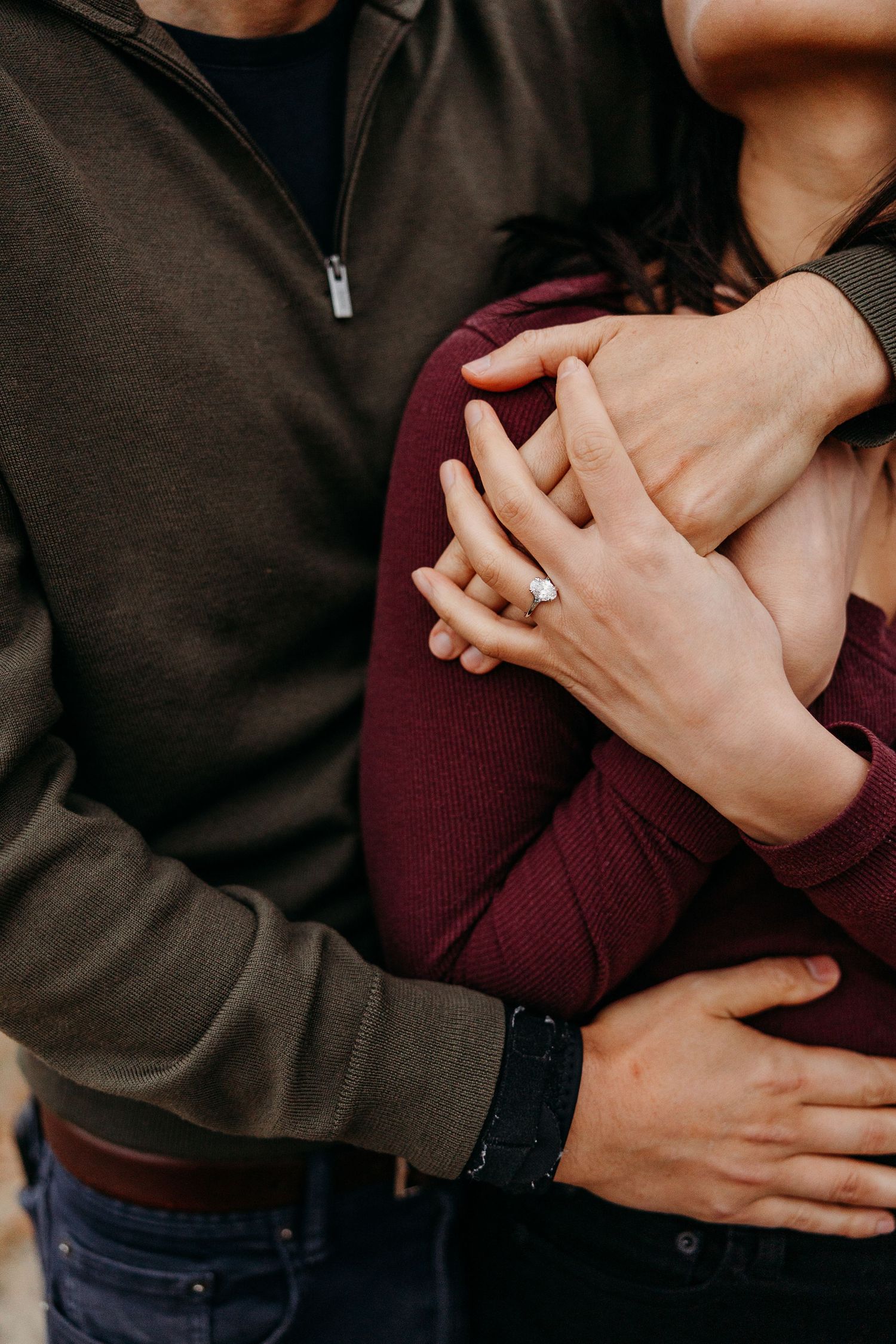 Close-up view of two people embracing in dark clothing showing only their torsos and hands.