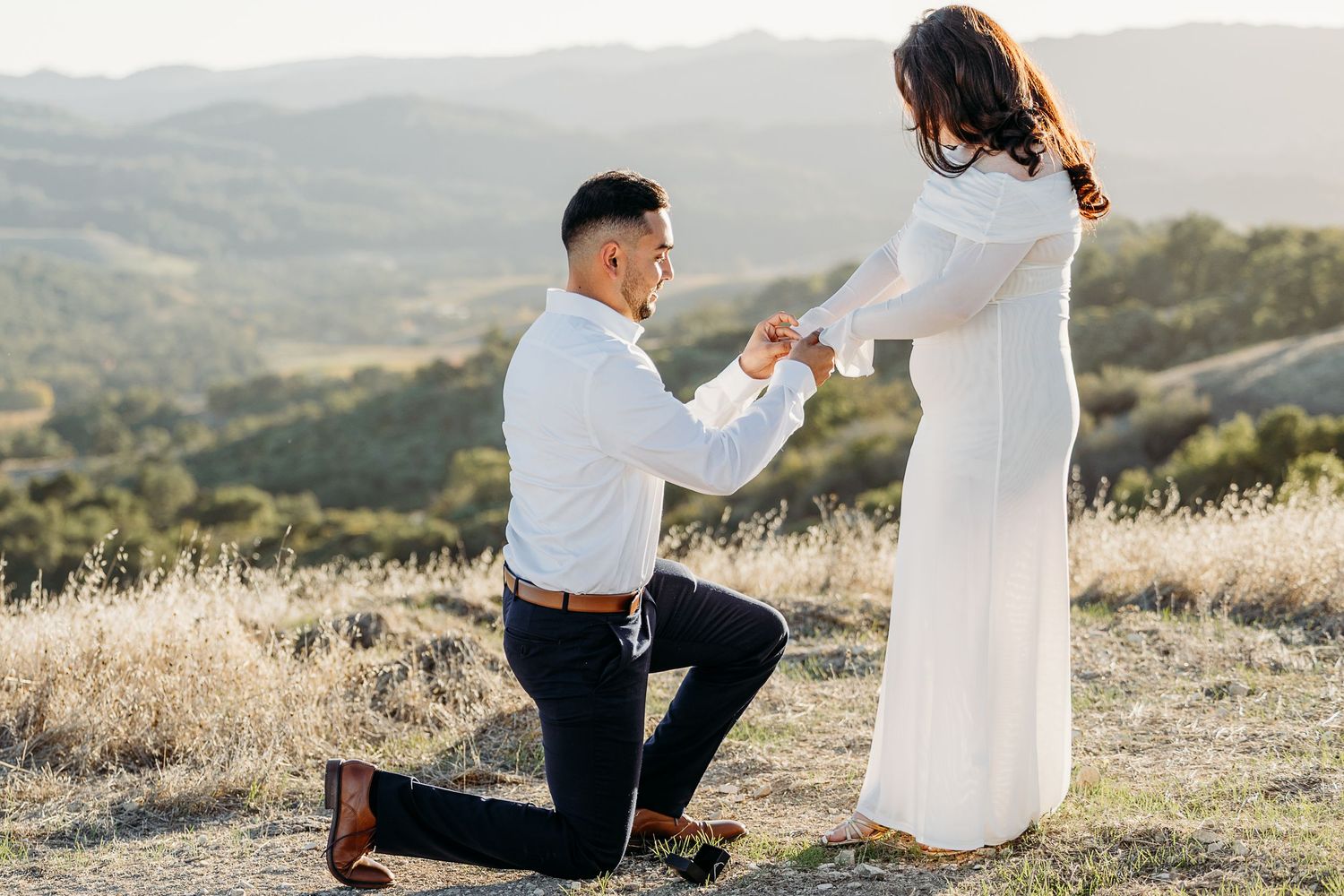 A romantic proposal moment on a hilltop during golden hour with mountains in the background.