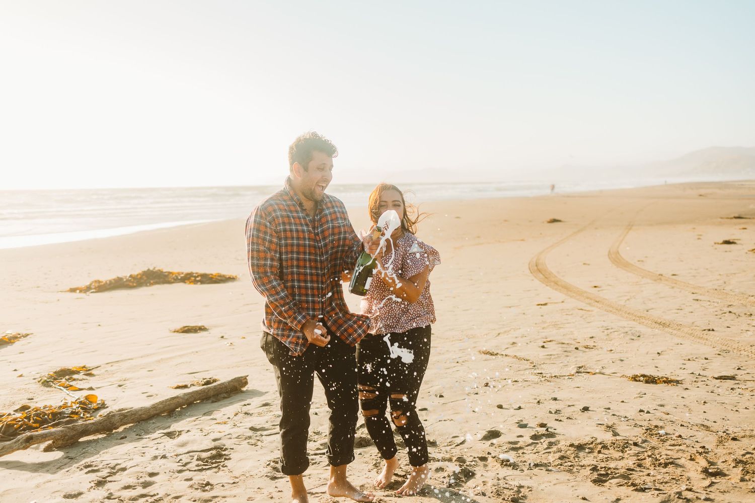 Couple celebrating their engagement on sandy beach during golden hour.