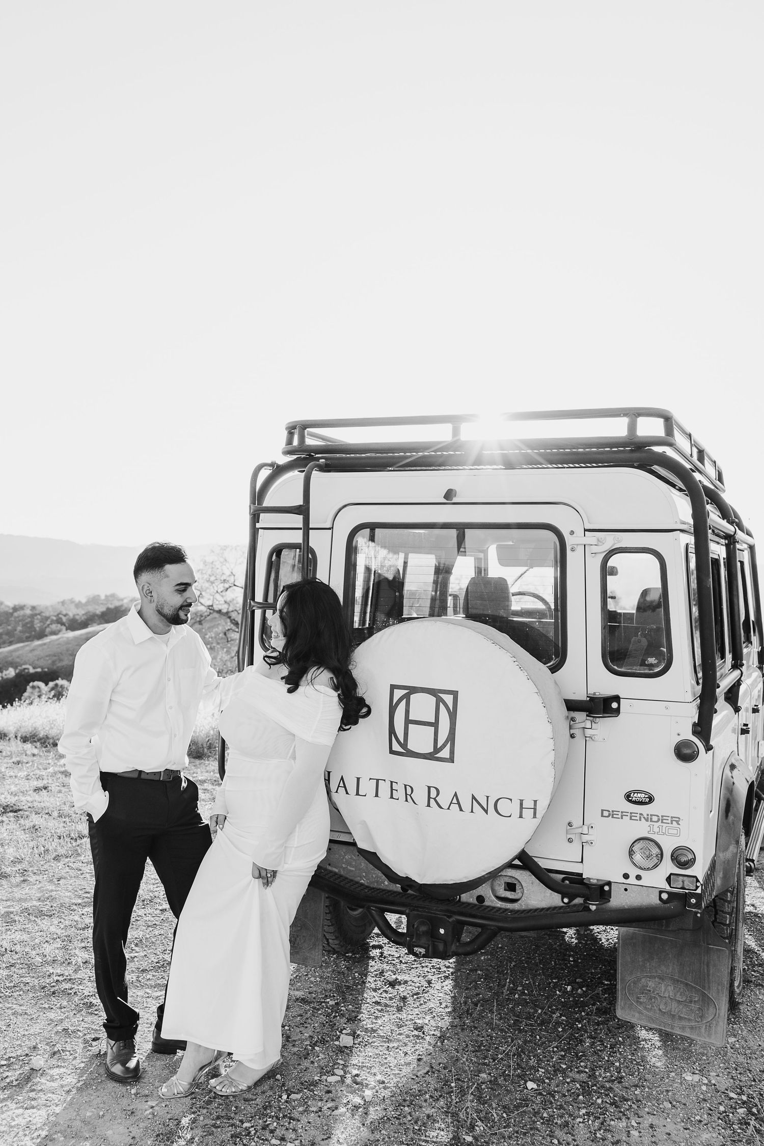 Black and white photo series showing a bride and groom with vintage Land Rover Defenders in a desert landscape setting.