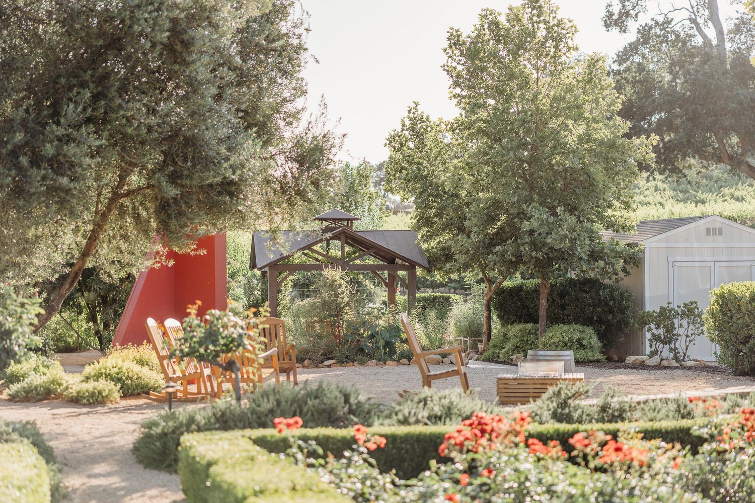 Tranquil garden landscape with orange flowers, stone path, and wooden arch surrounded by lush greenery and trees.