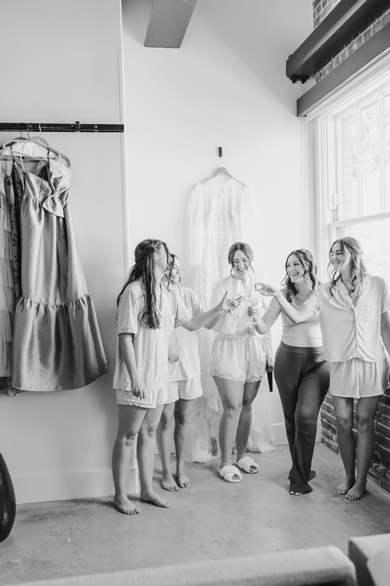 Group getting ready in a bright room with bridesmaid dresses hanging.