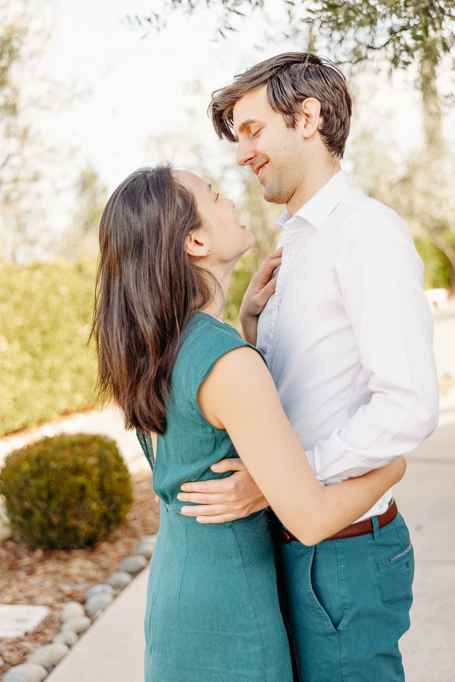 Romantic couple in coordinating teal and white outfits embrace outdoors in soft natural lighting.