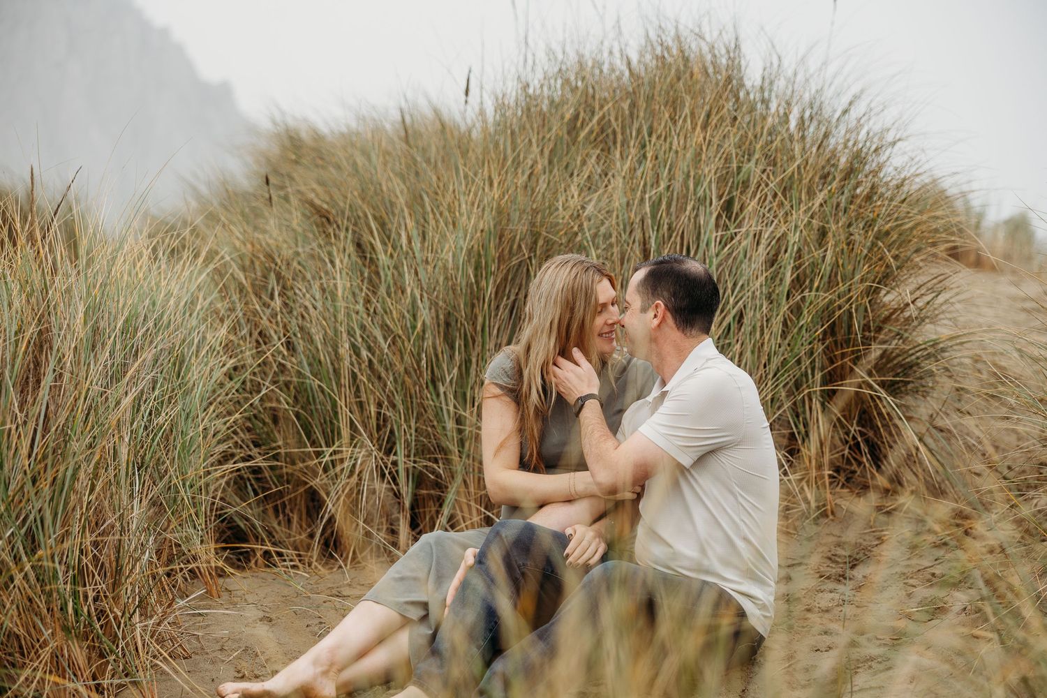 Candid photo of couple sharing intimate moment sitting together in beach grass landscape.