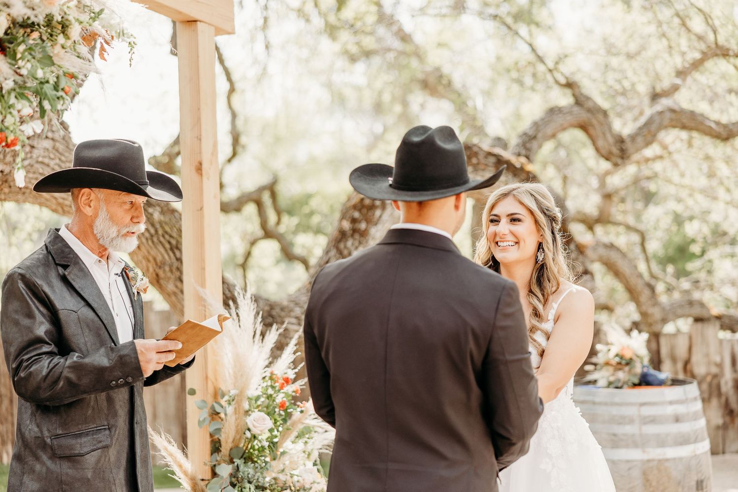 Outdoor wedding ceremony under rustic wooden arch with countryside backdrop.