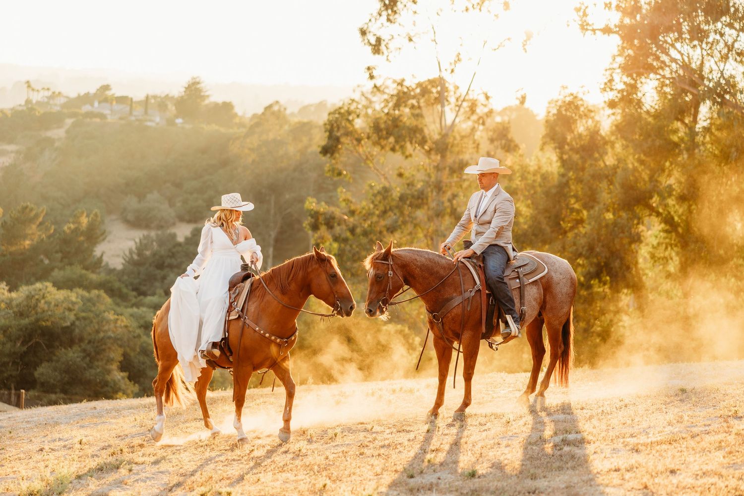 Two riders on horseback meet at sunset on a scenic hilltop trail.