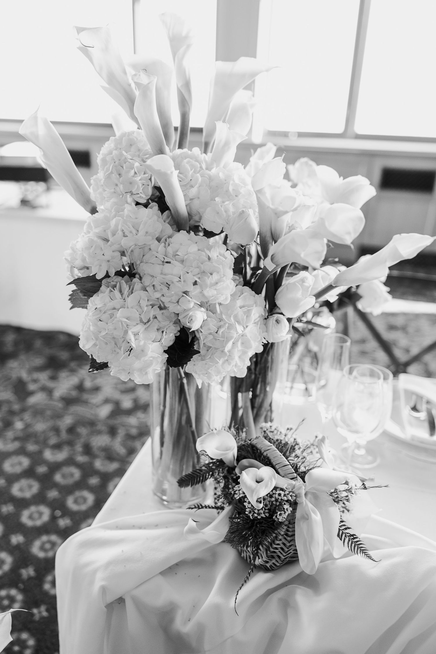 Elegant white floral centerpieces with hydrangeas arranged in glass vases on a white tablecloth at a formal event.