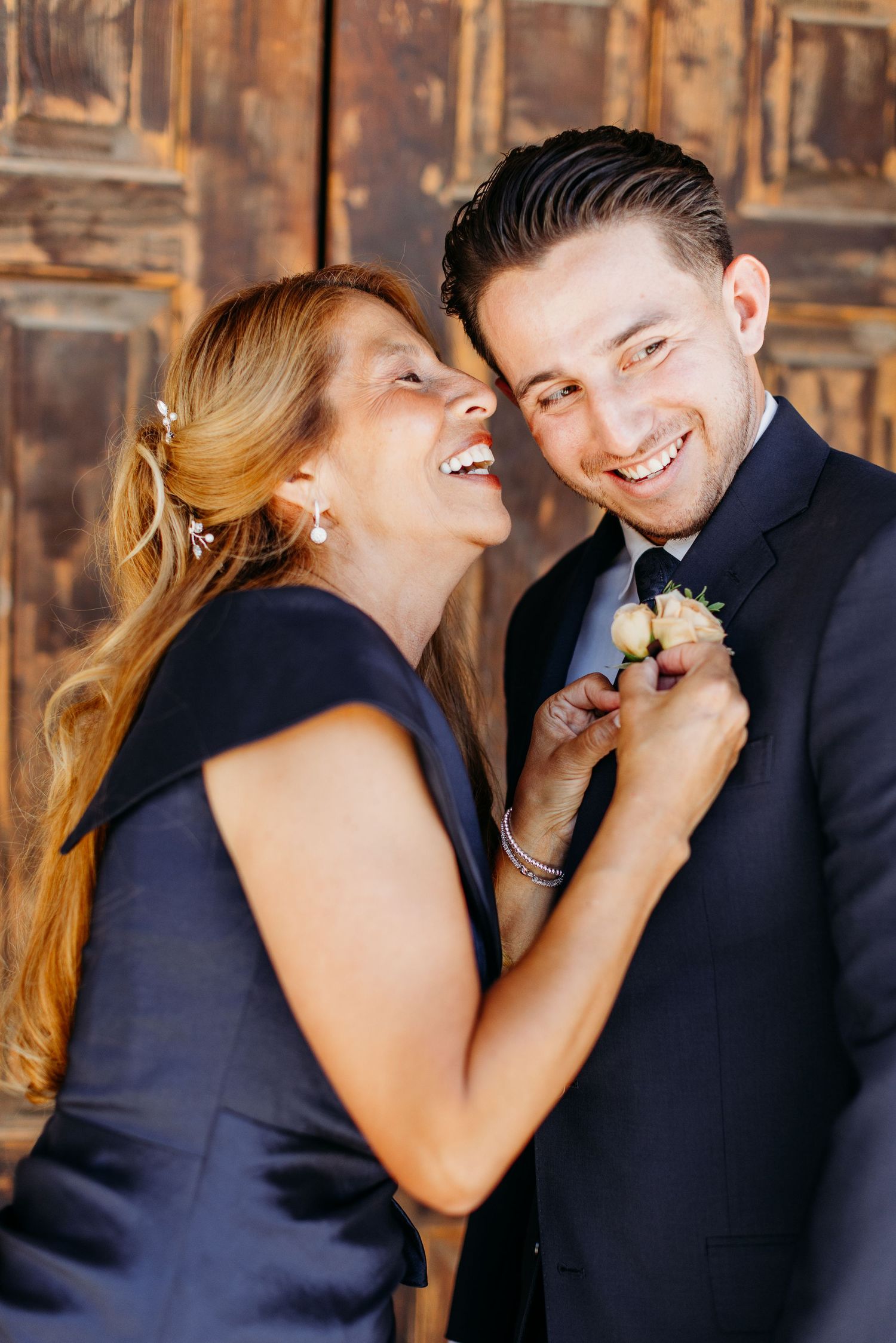 A couple shares a joyful moment together in formal attire against a rustic wooden wall background.