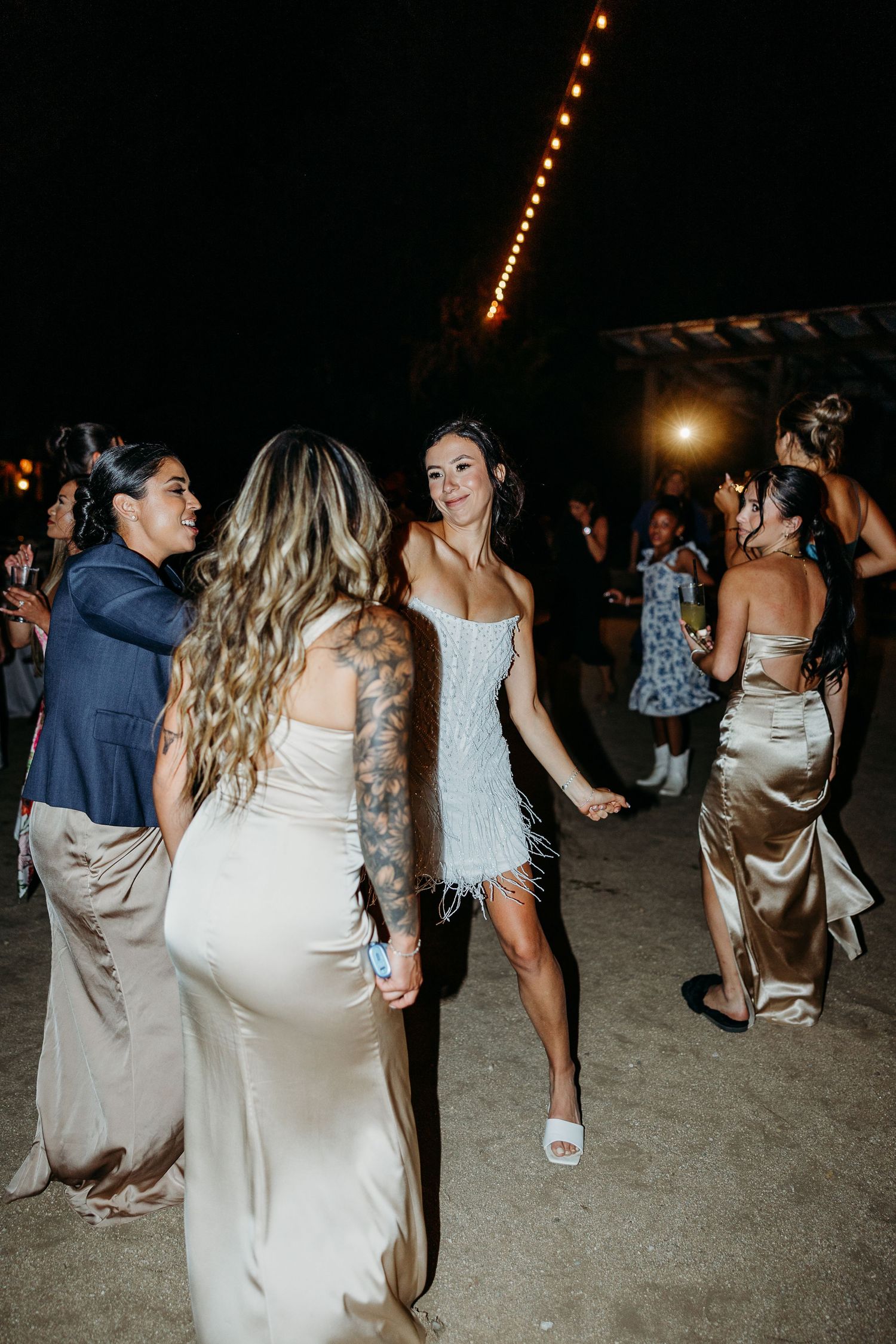 Lively dance floor scene at wedding reception with string lights overhead.