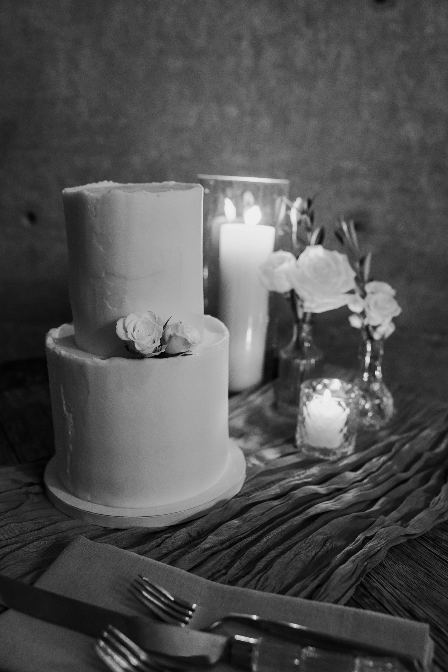 A minimalist white two-tier wedding cake with floral decorations and candles in black and white.