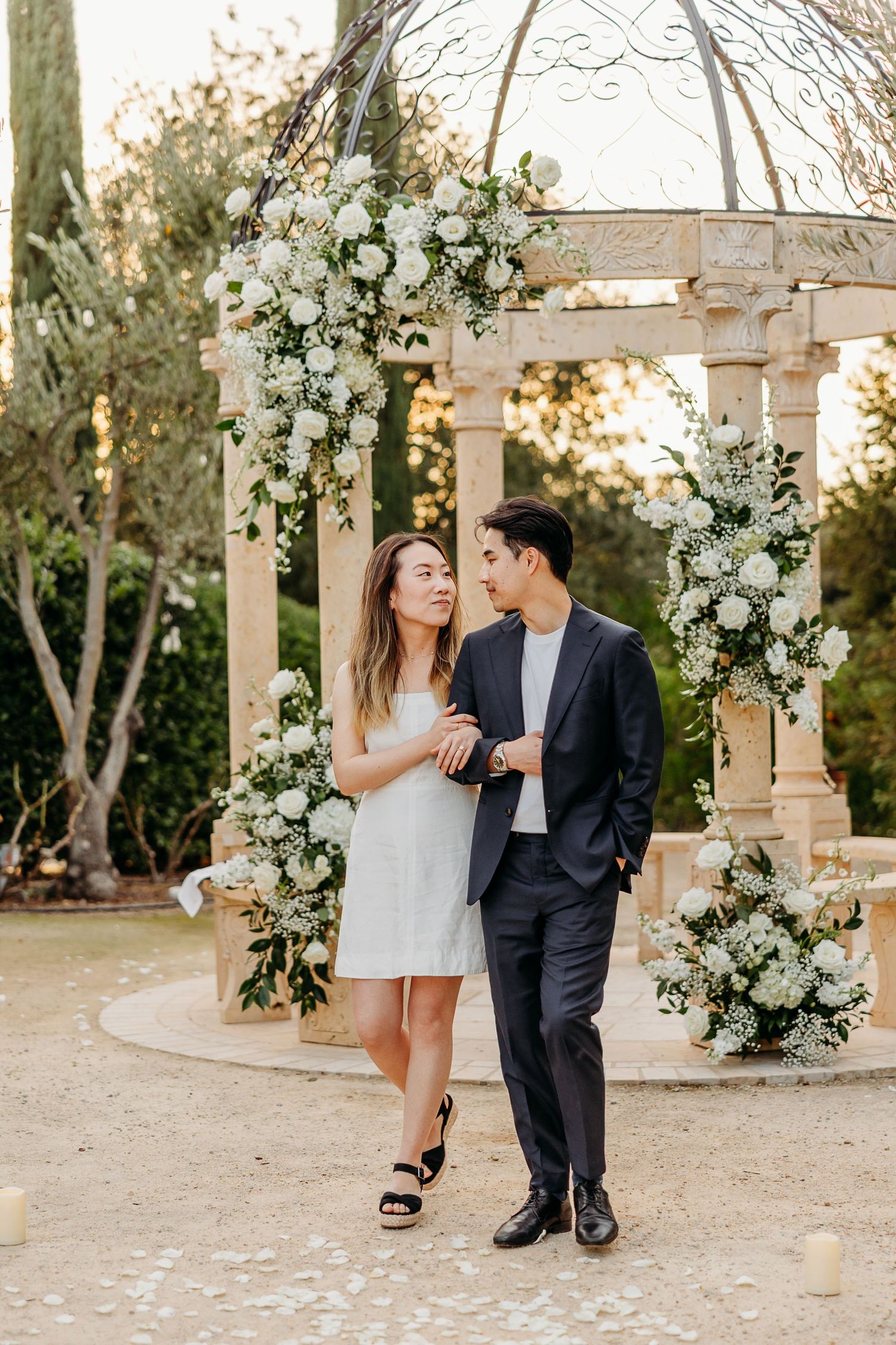 Engagement photos captured in garden setting with white floral arrangements and stone columns.