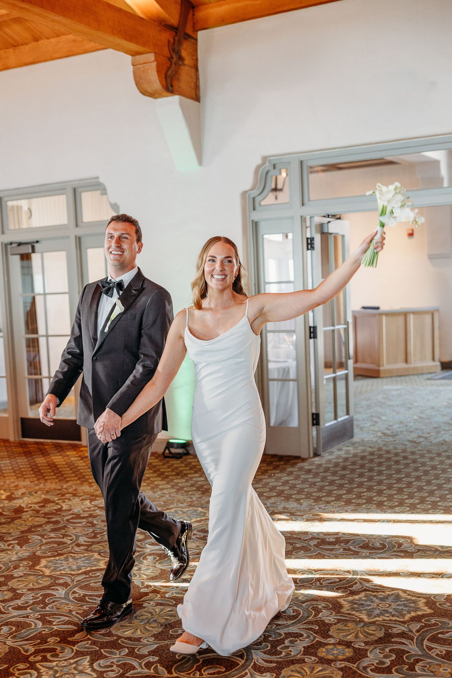 Wedding couple dancing and twirling in a sunlit room with wooden beams and patterned carpet.