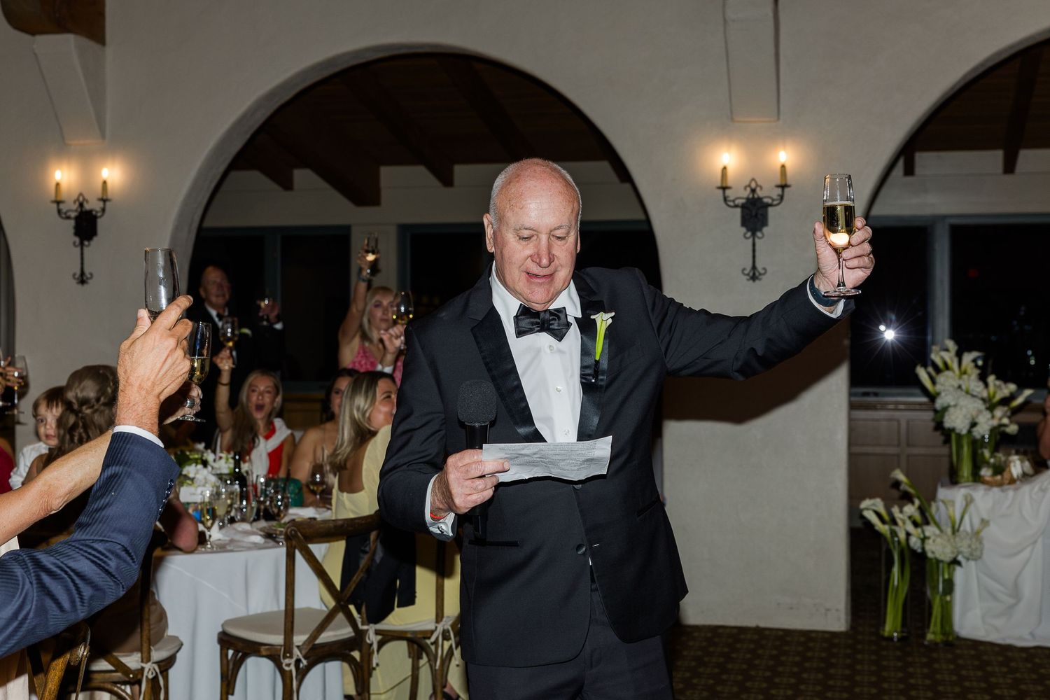 Wedding guests raise glasses during evening reception toasts.