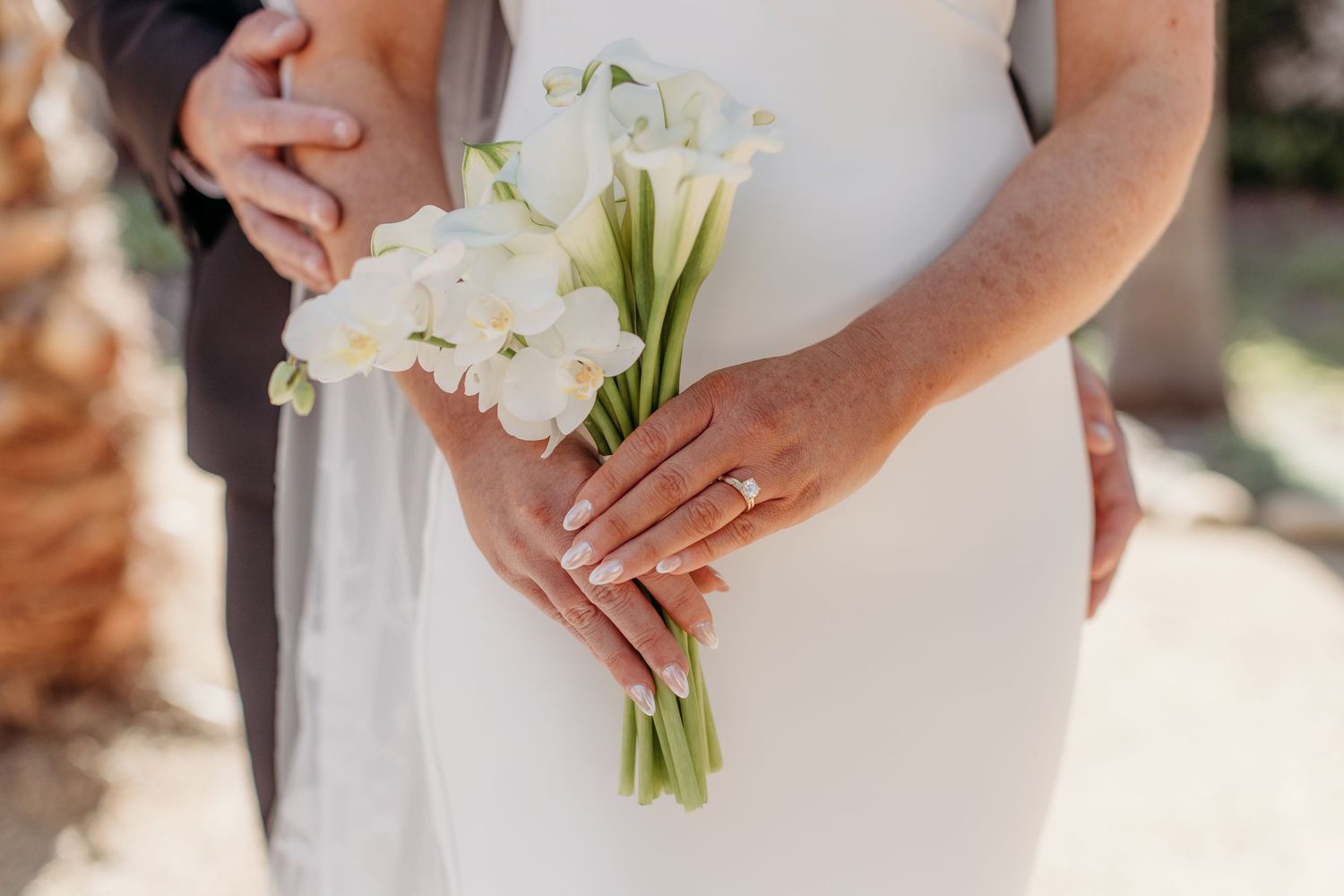 Close-up of wedding bouquet with white calla lilies being held by hands wearing elegant rings.
