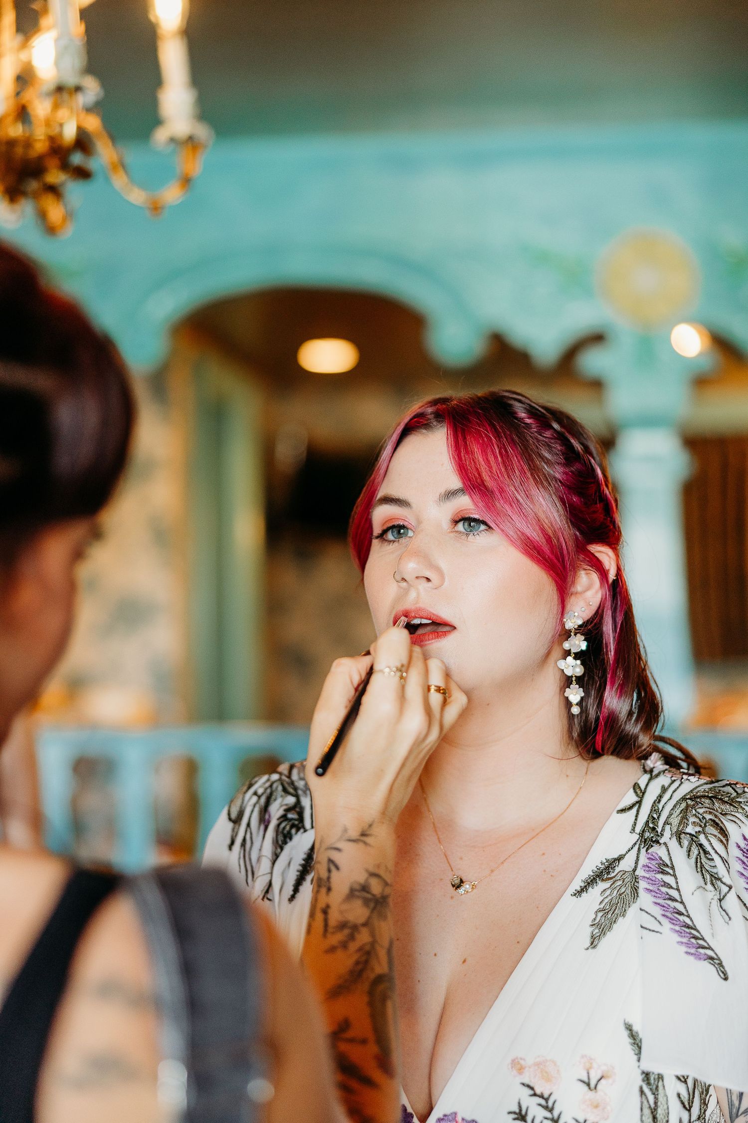Series of images showing makeup application in a turquoise-tinted room with vibrant pink hair details.