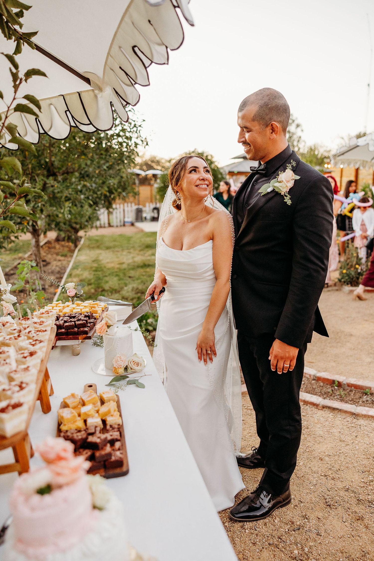 Newlyweds sharing a moment near their wedding dessert table at an outdoor reception.