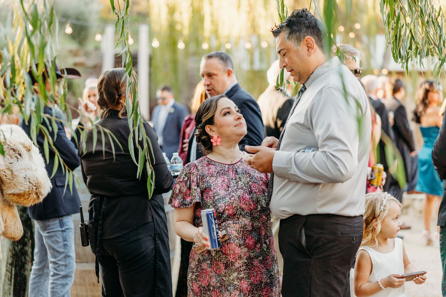 Wedding guests mingle during outdoor cocktail hour under willow trees.